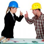 a girl and a man in helmets stand opposite each other with their index fingers raised