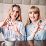 Two girls in a cafe show hearts with their hands