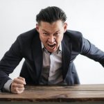 A man in a business suit hits the table with his hand and screams