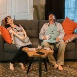 Уставшая семейная пара в домашней одежде сидит на диване с чашками чая