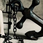 A woman is chained by her leg to a large anchor